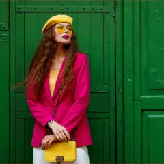Kobieta w fuksjowym żakiecie, żółtym beretce i okularach, z żółtą torebką. Taki outfit to kwintesencja stylu!