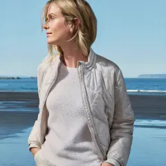 Kobieta w beżowej kurtce z pikowanego materiału z dodatkiem elastanu, stojąca na plaży.
