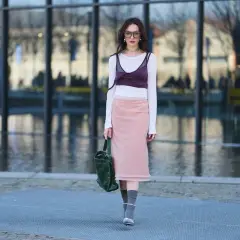 Dziewczyna w stylu balletcore, w różowej spódnicy i białej bluzce z bordowym topem, idzie ulicą.