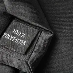 Czarna metka z napisem "100% POLYESTER" na tle eleganckiego materiału. Czy poliester jest zdrowy? To pytanie nurtuje wielu konsumentów.