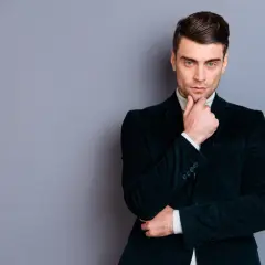 Elegancki mężczyzna w granatowym, sztruksowym garniturze, z dłonią na brodzie, zastanawia się nad czymś.
