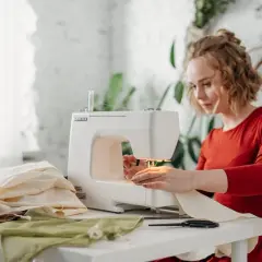 Kobieta szyje na maszynie, obok stosy materiałów, w tym delikatny modal.