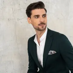 Elegancki mężczyzna w granatowej marynarce z ozdobną poszetką. Biała koszula z kołnierzykiem typu stójka podkreśla jego styl.