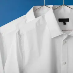 Dwie białe koszule wiszą na wieszakach. Dowiedz się, jak wybielić białe ubrania, aby wyglądały jak nowe.