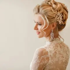 Elegancka fryzura wieczorowa blondynki z perłową ozdobą i długimi kolczykami.