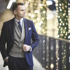 Elegancki mężczyzna w granatowym garniturze i szarej kamizelce, gotowy na wieczorne wyjście. Jego strój koktajlowy męski podkreśla jego styl.