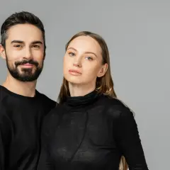 Para, która wygląda jakby mogła nosić ubrania unisex. Mężczyzna z brodą i kobieta z długimi włosami, oboje w czarnych, prostych ubraniach.