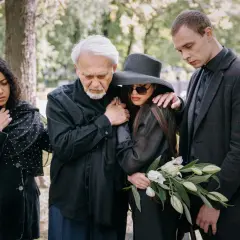 Smutna rodzina na cmentarzu. Eleganckie, ciemne stroje, jak się ubrać na pogrzeb, podkreślają żałobę.