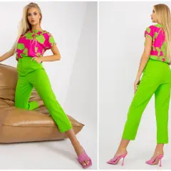 Modelka w stylizacji z bluzką w intensywny wzór i spodniami w kolorze limonkowym, siedząca na brązowej poduszce.
