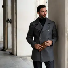 Elegancki mężczyzna w szarej bosmance i czarnym golfie, trzymający brązowe rękawiczki.