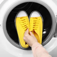 Ręka wkłada żółte trampki do bębna suszarki. Czy można suszyć buty w suszarce? Sprawdź instrukcję!