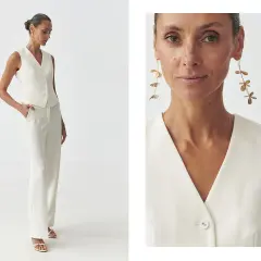 Elegancka kobieta prezentuje, jak nosić kamizelkę damską w stylizacji z białymi spodniami. Długie kolczyki dodają szyku.