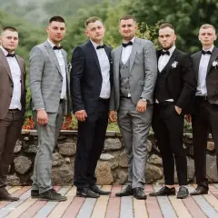 Sześciu mężczyzn w eleganckich garniturach, idealnych na wesele. Różne odcienie szarości, granatu i brązu, każdy z panów prezentuje się stylowo.
