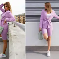 Kobieta w stylizacji z marynarką i kolarkami w odcieniu barwy fioletowej, z miętową torebką i kolorowymi sneakersami.