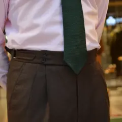 Elegancki mężczyzna w różowej koszuli i brązowych spodniach. Krawat sięga idealnie do klamry paska.