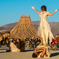 Akrobaci na pustyni podczas Burning Man. W tle charakterystyczna konstrukcja i tłum ludzi.