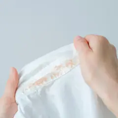 Dłonie trzymają białą koszulę z widocznymi plamami. Dowiedz się, jak usunąć plamy z podkładu.
