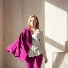 Młoda kobieta w eleganckim garniturze w intensywnym, **magenta kolorze**. Marynarka narzucona na ramię, spodnie podkreślają sylwetkę.