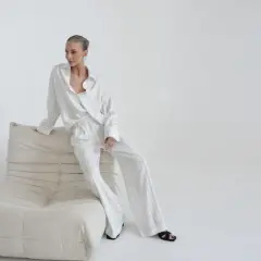 Kobieta w eleganckim, pasiastym komplecie, uosobienie quiet luxury, siedzi na kremowej sofie.