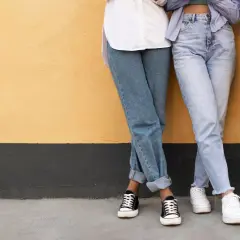 Trzy osoby w jeansach, w tym jeansy straight, stoją przy żółtej ścianie.