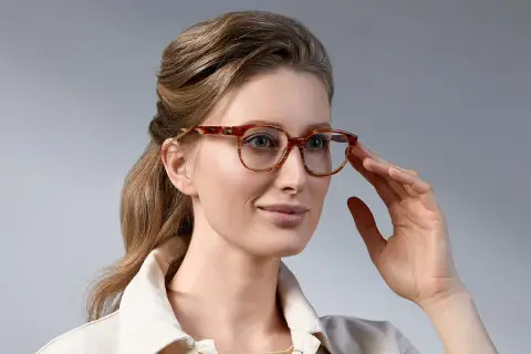 Elegancka kobieta z upiętymi włosami, prezentująca stylowe fryzury do okularów damskie. Jej spojrzenie podkreślają modne oprawki.