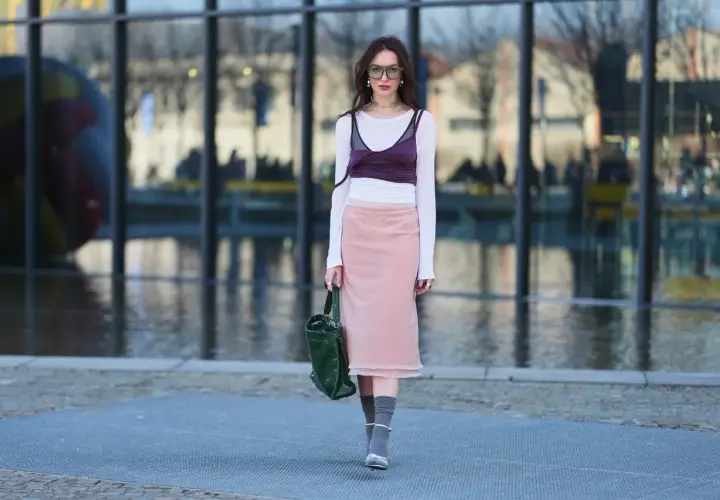 Dziewczyna w stylu balletcore, w różowej spódnicy i białej bluzce z bordowym topem, idzie ulicą.