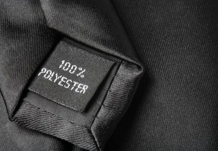 Czarna metka z napisem "100% POLYESTER" na tle eleganckiego materiału. Czy poliester jest zdrowy? To pytanie nurtuje wielu konsumentów.