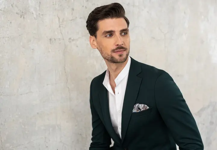 Elegancki mężczyzna w granatowej marynarce z ozdobną poszetką. Biała koszula z kołnierzykiem typu stójka podkreśla jego styl.