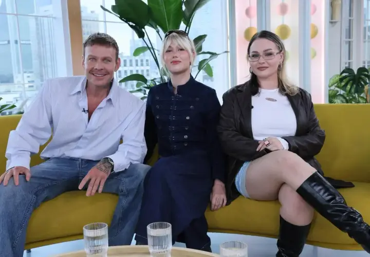 Trzy osoby siedzą na kanapie. Mężczyzna w koszuli i jeansach, przypominający styl lat 2000 moda męska, obok dwie kobiety w modnych stylizacjach.