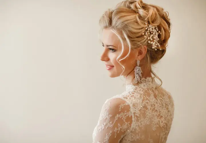 Elegancka fryzura wieczorowa blondynki z perłową ozdobą i długimi kolczykami.