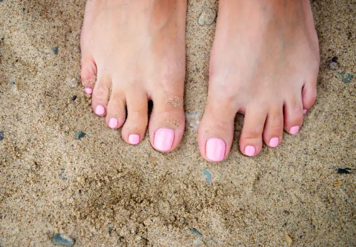 Stopy na piasku z różowym, modnym pedicure. Idealne na lato.