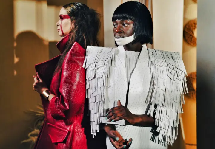 Dwie modelki w awangardowych kreacjach haute couture. Jedna w czerwonej, łuskowej marynarce, druga w białej z frędzlami.