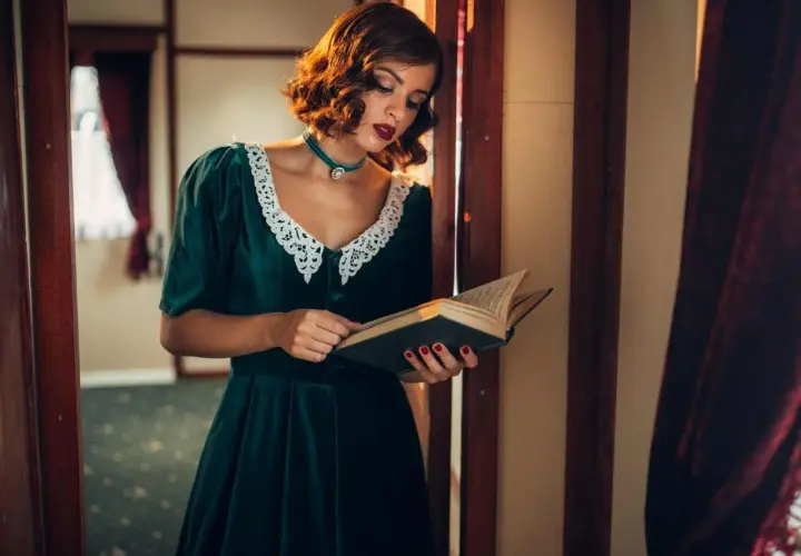 Elegancka kobieta w sukni z lat 40. XX wieku, z koronkowym kołnierzykiem, czyta książkę.