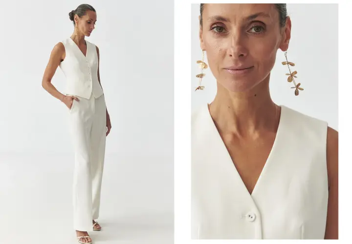 Elegancka kobieta prezentuje, jak nosić kamizelkę damską w stylizacji z białymi spodniami. Długie kolczyki dodają szyku.