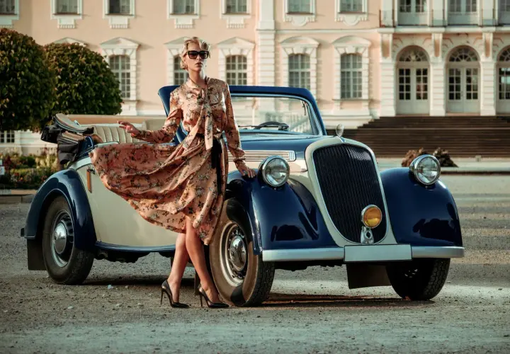 Elegancka kobieta w kwiecistej sukience i szpilkach przy zabytkowym kabriolecie. Stylowe lata 20. w pełnej krasie.