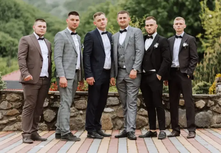 Sześciu mężczyzn w eleganckich garniturach, idealnych na wesele. Różne odcienie szarości, granatu i brązu, każdy z panów prezentuje się stylowo.