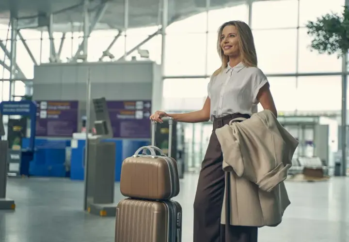 Elegancka kobieta w stylowym ubraniu do samolotu, z walizkami i płaszczem, czeka na lotnisku.