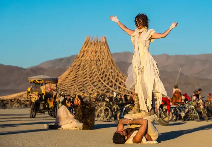 Akrobaci na pustyni podczas Burning Man. W tle charakterystyczna konstrukcja i tłum ludzi.