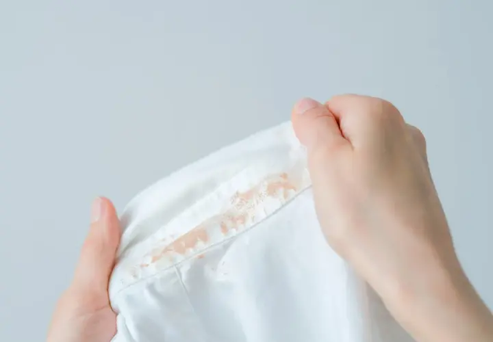 Dłonie trzymają białą koszulę z widocznymi plamami. Dowiedz się, jak usunąć plamy z podkładu.