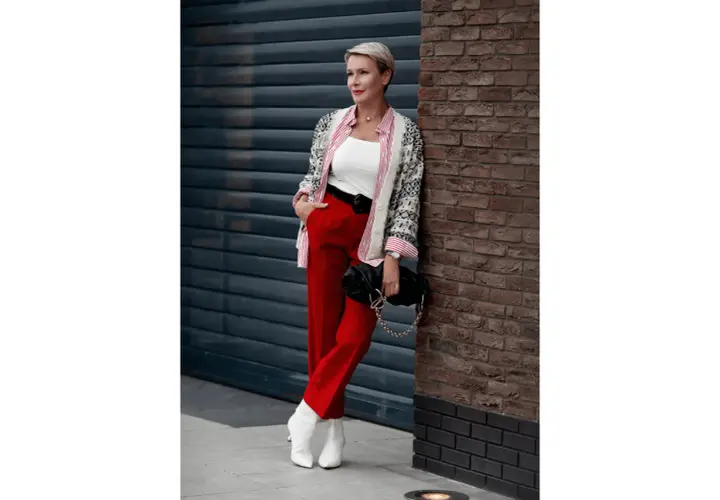 Elegancka kobieta w czerwonych spodniach i wzorzystej marynarce, z czarną torebką na łańcuszku. Stylowe czerwone spodnie stylizacje.