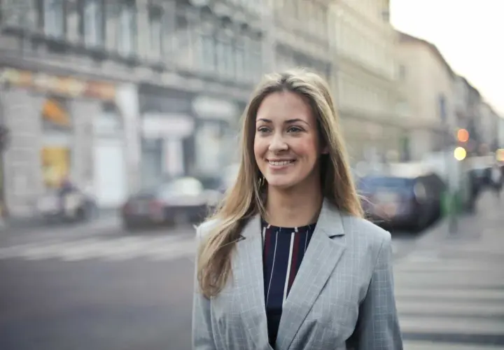 Uśmiechnięta kobieta w marynarce na tle miasta. Jej pozytywne renee opinie o życiu są widoczne w promiennej twarzy.