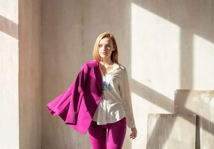 Młoda kobieta w eleganckim garniturze w intensywnym, **magenta kolorze**. Marynarka narzucona na ramię, spodnie podkreślają sylwetkę.