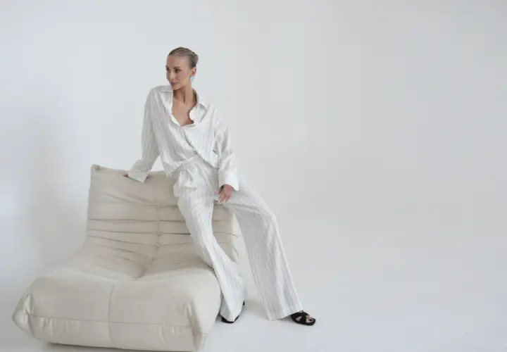 Kobieta w eleganckim, pasiastym komplecie, uosobienie quiet luxury, siedzi na kremowej sofie.