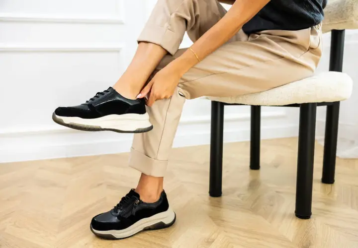 Kobieta poprawia czarne sneakersy na nogach. Dowiedz się, jak szybko wysuszyć buty, by znów cieszyć się komfortem.