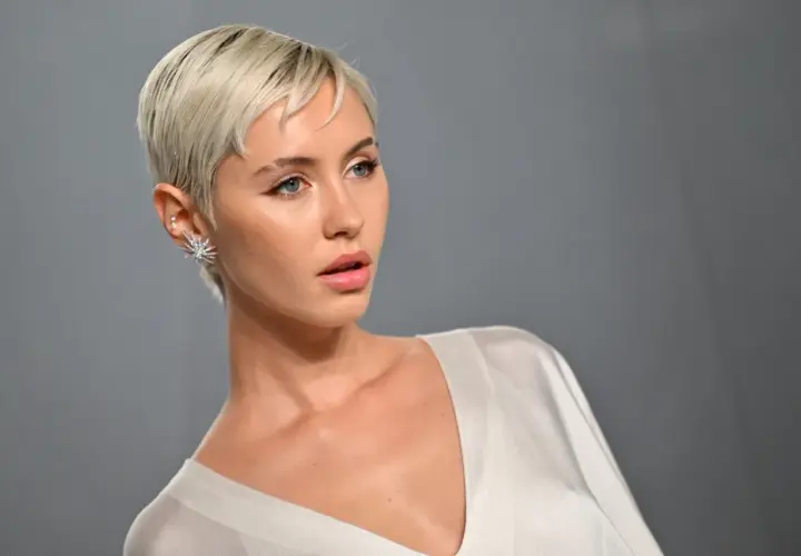Krótkie, blond włosy i wyraziste rysy twarzy. Stylizacja z błyszczącą biżuterią, idealna jako inspiracja fryzury dla grubych twarzy.