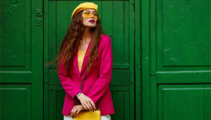Kobieta w fuksjowym żakiecie, żółtym beretce i okularach, z żółtą torebką. Taki outfit to kwintesencja stylu!