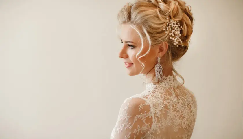 Elegancka fryzura wieczorowa blondynki z perłową ozdobą i długimi kolczykami.