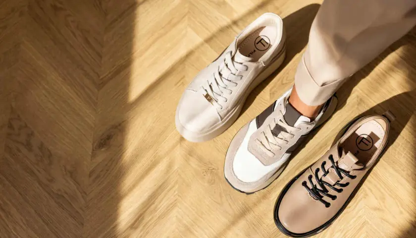 Beżowe sneakersy i półbuty na drewnianej podłodze. Idealne buty do cygaretek dla stylowej kobiety.