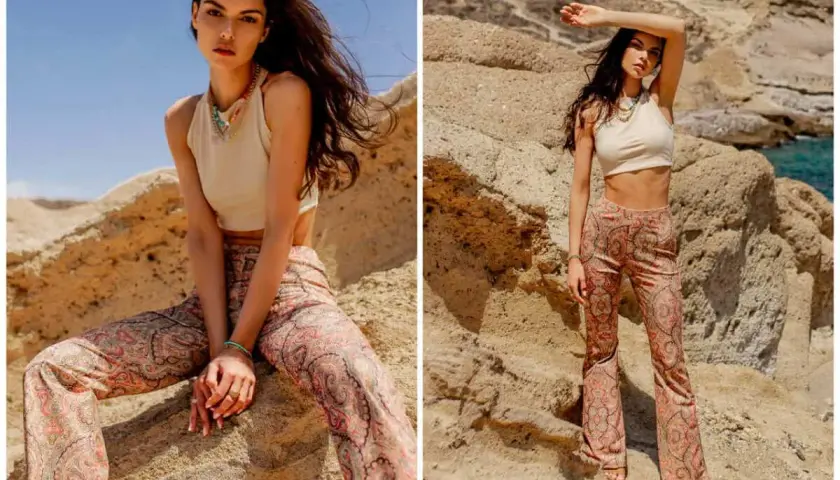 Modelka w beżowym topie i spodniach z orientalnym wzorem paisley, pozuje na tle skalistego krajobrazu.