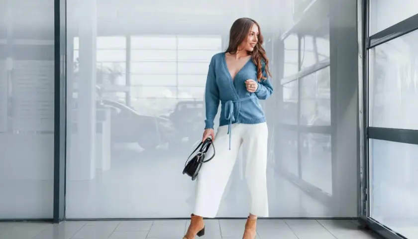 Kobieta w białych kulotach i błękitnym sweterku, zastanawia się, jakie buty do kulotów będą najlepsze. Eleganckie botki na obcasie.